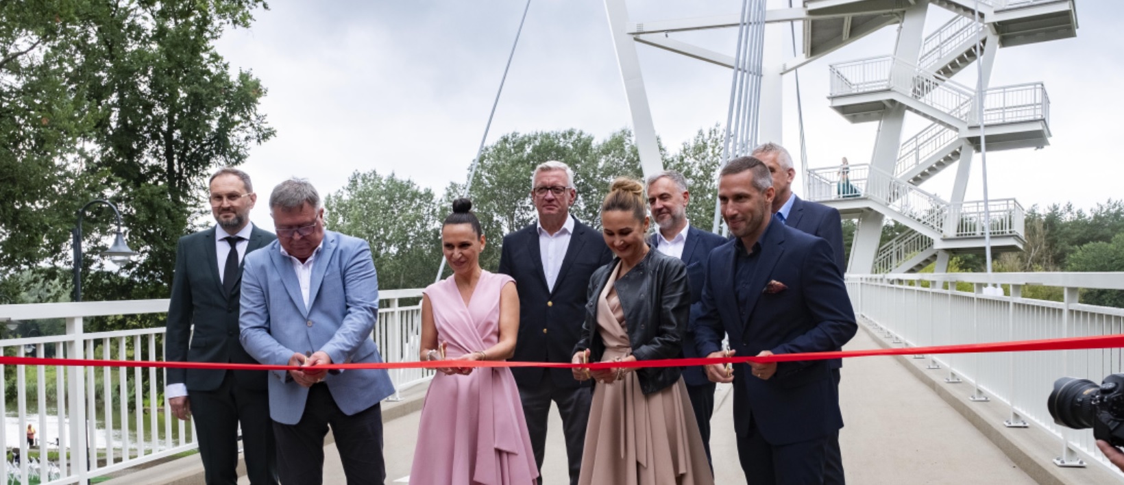 Kladka_Owinska_otwarcie_2023 Fotografia przedstawiająca grupę ludzi przecinających wstęgę na tle kałdki przez Wartę